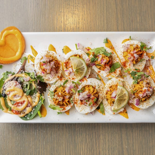 A white platter of Indian deviled eggs, garnished with spices, red onion, cilantro, and lime.