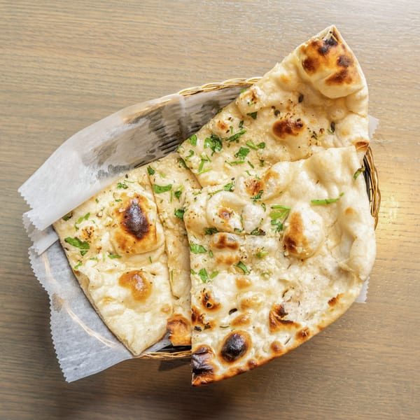Basket of warm, golden-brown garlic naan bread, garnished with fresh green herbs, on a wooden table.