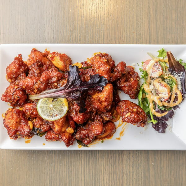 Indian chili chicken with a lime slice and a small side salad on a white rectangular plate.