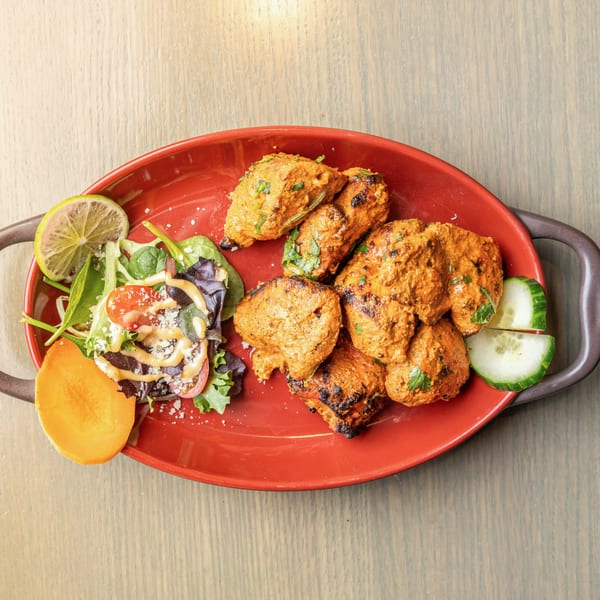 Bowl O Biryani's chicken tikka, salad with dressing, lime, and cucumber on a red platter.