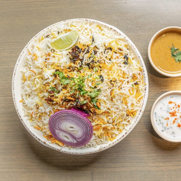 A large bowl of biryani rice with lime, red onion, and cilantro, served with two side sauces.