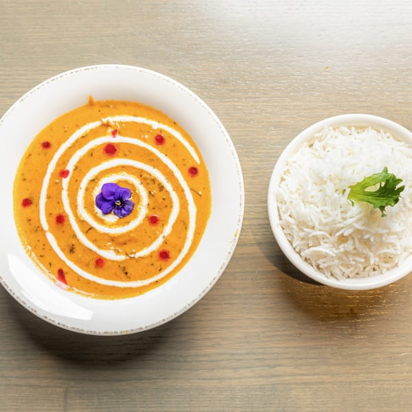 Overhead view of a bowl of orange curry with a cream swirl and a side of white rice.