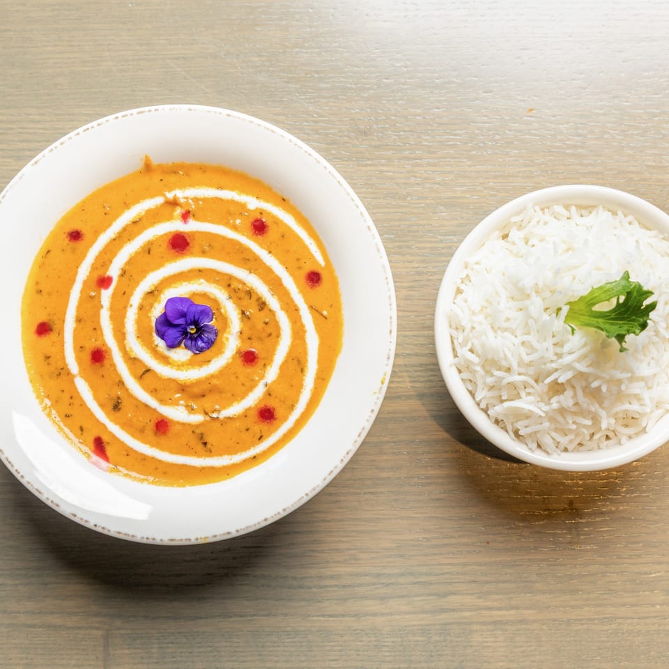 Overhead view of a bowl of orange curry with a cream swirl and a side of white rice.