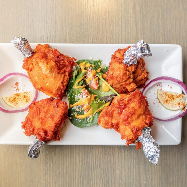 Four crispy red chicken lollipops with foil-wrapped bones, served with a side salad and red onion.