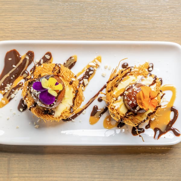 Two Indian desserts, Gulab Jamun, in crispy nests with chocolate, caramel, nuts, and edible flowers.
