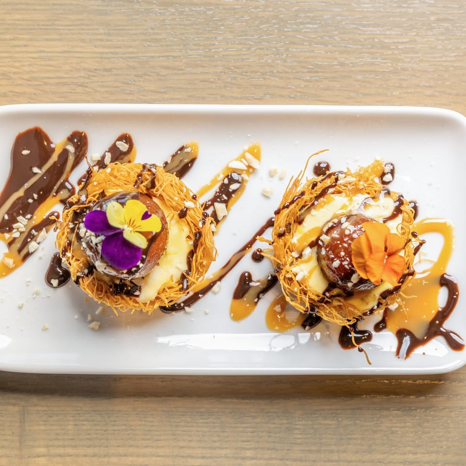 Two Indian desserts, Gulab Jamun, in crispy nests with chocolate, caramel, nuts, and edible flowers.