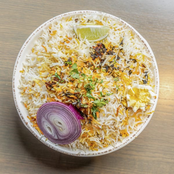 Overhead view of a Bowl O Biryani dish with rice, lime, red onion, and egg.